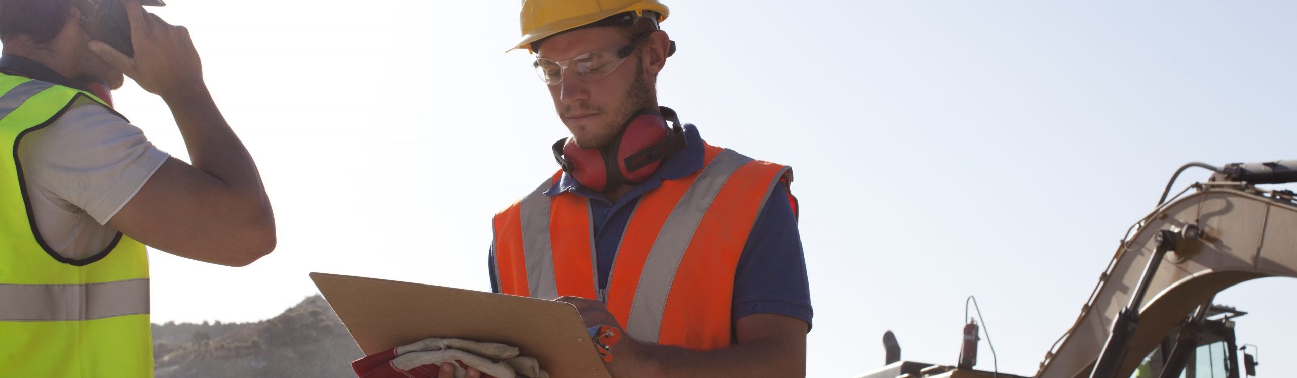 Two workers at a construction workplace Two employees at a construction site, wearing orange and yellow work-jackets