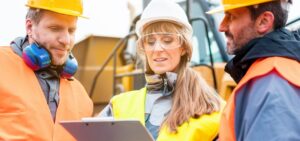 Three workers in a quarry discussing in front of heavy machinery looking at plan