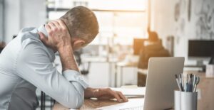 Man holding sore neck while using notebook computer. He sitting at table. Sick worker concept