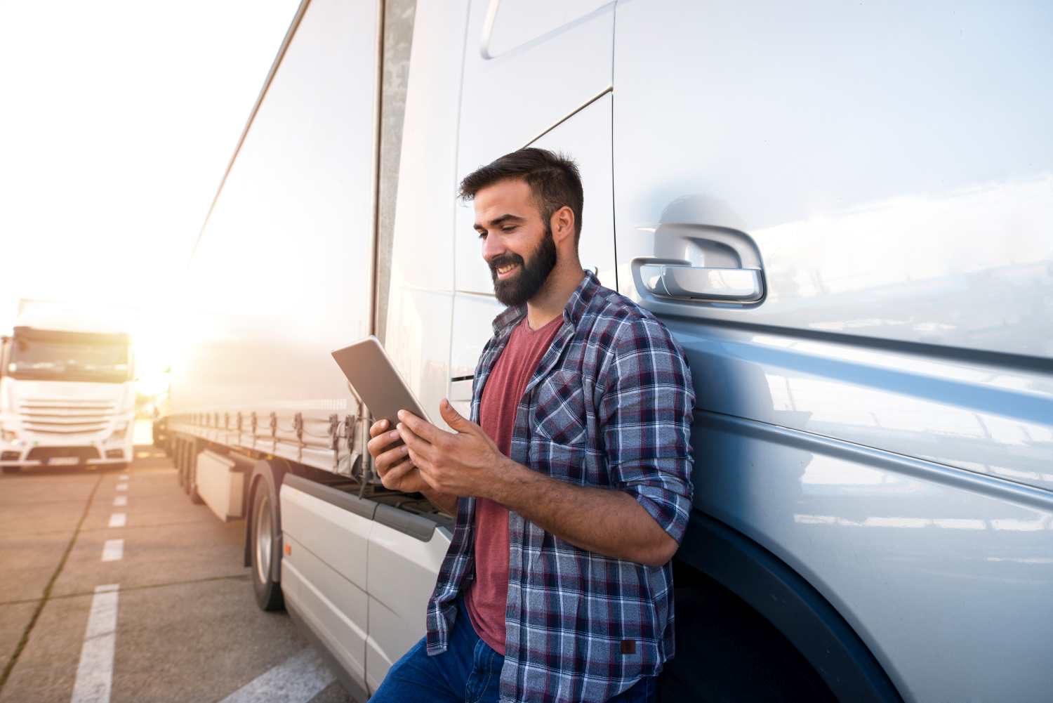 Man fills out truck pre trip inspection form digitally on his tablet while leaning on his truck on a sunny day. 