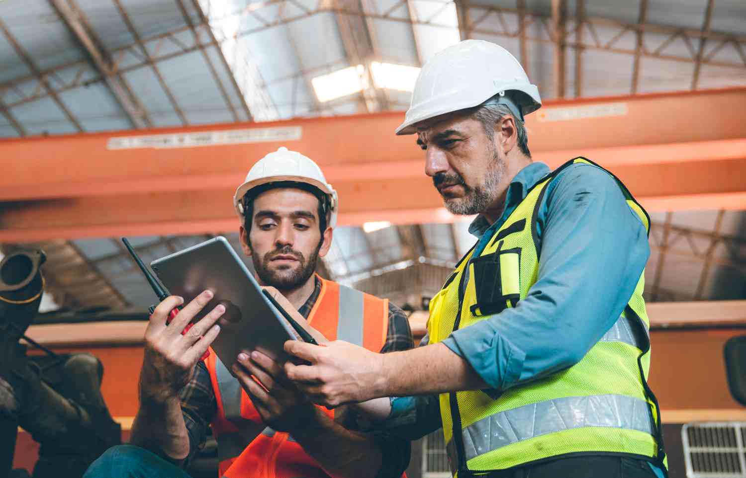 Two Gentlemen view safety training course on tablet in factory with gantry crane in the backround.